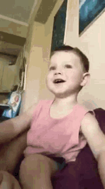 a little boy in a pink tank top is sitting on a couch and making a funny face .