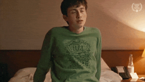 a young man wearing a green shirt is sitting on a bed .