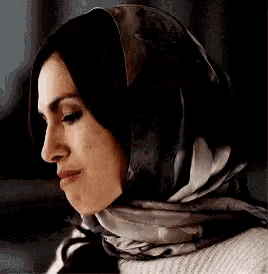 a woman is wearing a scarf around her head and a sweater .