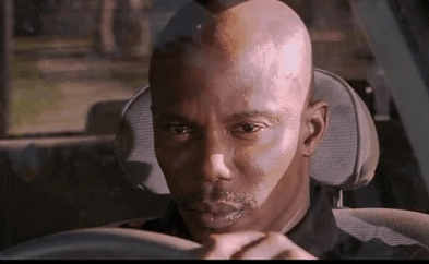 a bald man is sitting in the driver 's seat of a car and looking at the camera .