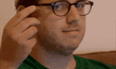 a man wearing glasses and a green shirt is holding something to his face
