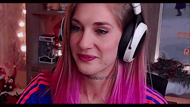 a woman with pink hair is wearing headphones and a choker necklace .
