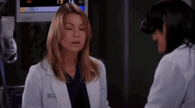 a woman in a lab coat is talking to another woman in a hospital .