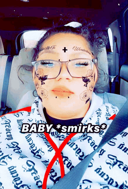 a woman with a tattoo on her face is sitting in a car with the words baby * smirks * above her