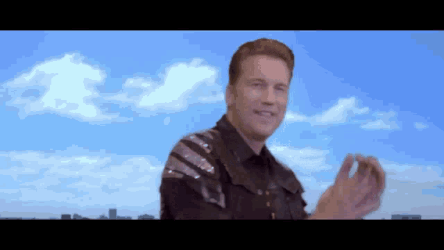 a man in a sequined jacket is clapping in front of a blue sky
