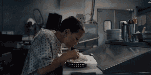a little girl in a hospital gown is eating a sandwich