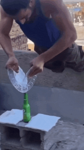 a man in a blue tank top is pouring liquid into a green bottle ..