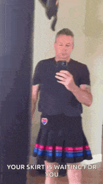 a man is taking a selfie in front of a mirror while wearing a skirt .