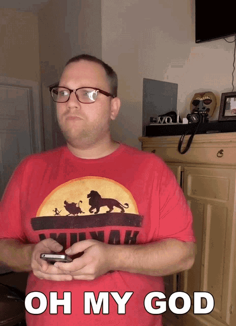 a man wearing a red shirt with a lion on it is holding a cell phone and says oh my god