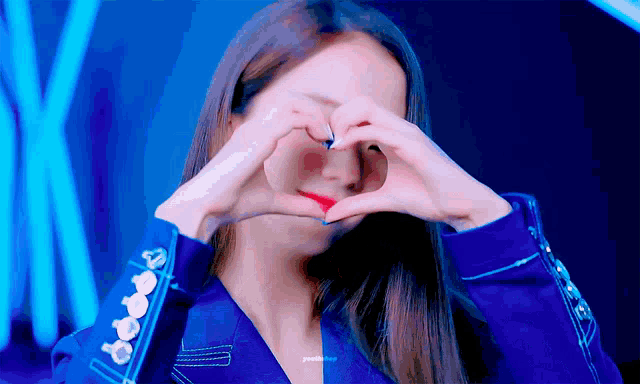 a woman in a blue jacket making a heart with her hands