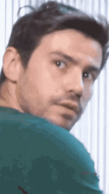 a man with a beard and a green shirt is looking over his shoulder