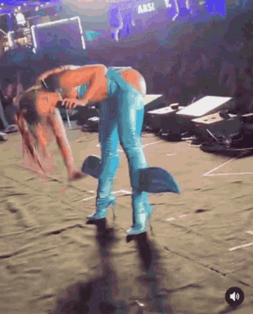 a woman in blue pants and heels is bending over on the floor while holding a microphone .