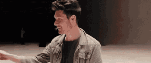 a man in a denim jacket is standing in a dark room with his arms outstretched .