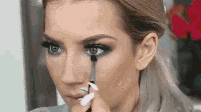 a close up of a woman applying makeup to her face