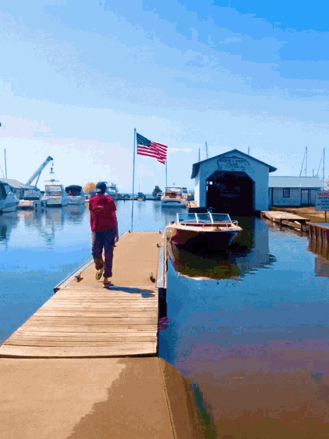 a man walks down a dock in front of a boat shed that says ' yacht & yacht ' on it