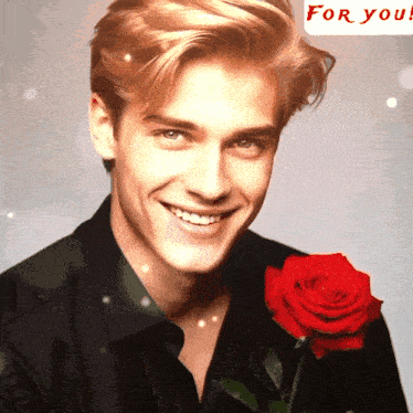 a man is smiling while holding a red rose in front of a for you banner