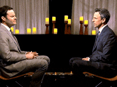 a man in a suit and tie sits next to another man in a chair