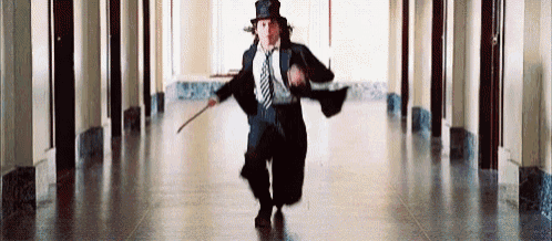 a man in a top hat and tie is running down a hallway holding a cane .