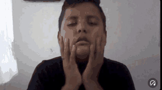 a young boy is making a face with his hands on his face .