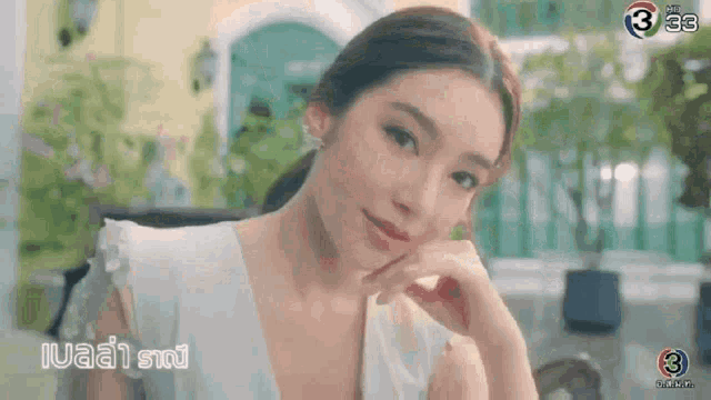 a woman in a white dress is sitting at a table looking at the camera .