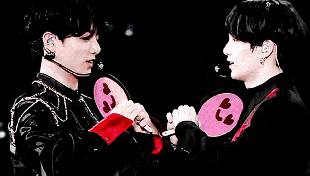 two young men are making a heart shape with their hands while wearing microphones .