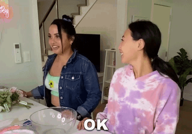 a woman in a tie dye sweatshirt says ok while standing next to another woman in a denim jacket