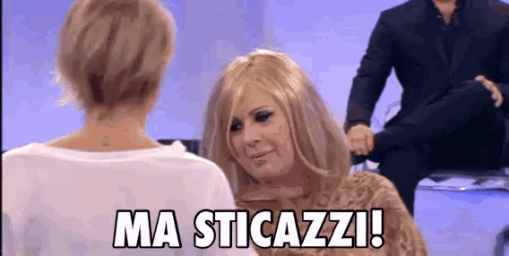a woman in a wig is talking to another woman while a man sits in the background and says ma sticazzi !