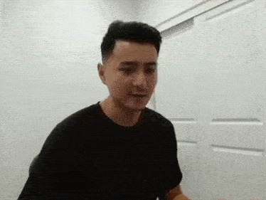 a man in a black t-shirt is standing in front of a white door in a room .