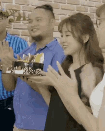 a woman in a black dress is holding a cake in front of a man in a blue shirt .