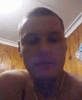 a shirtless man wearing a chain around his neck looks at the camera