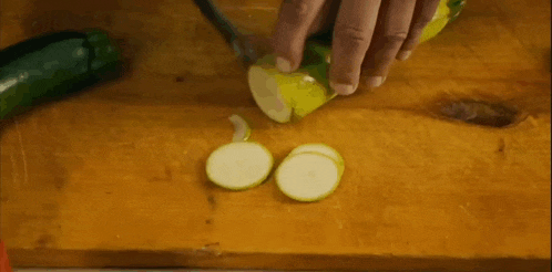 a person is cutting a zucchini on a cutting board with a knife .