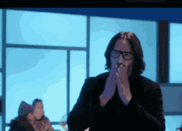 a man wearing glasses is clapping his hands in a dark room