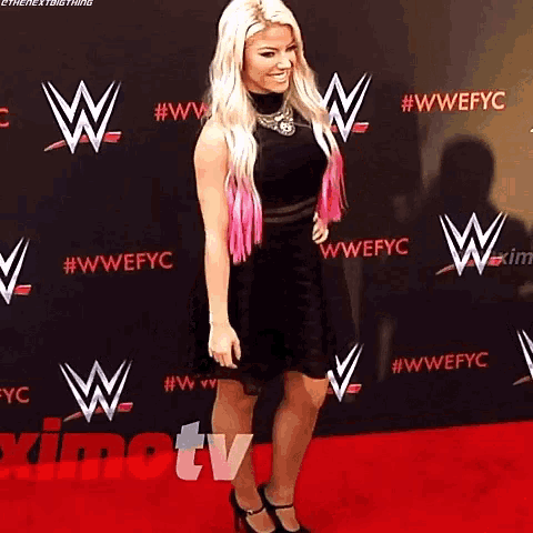 a woman in a black dress and pink hair is standing on a red carpet ..