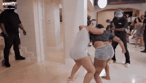 two women are fighting in a room with a man in a black shirt that says ' nowthistv '