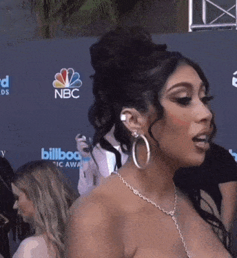 a woman wearing hoop earrings stands in front of a wall that says nbc on it