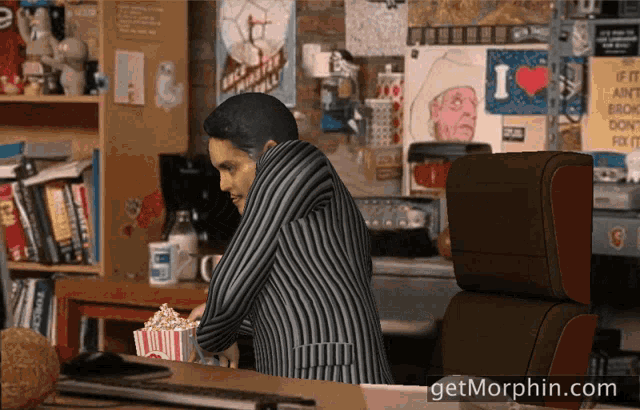 a man sits at a desk with a box of popcorn in front of him and the website getmorphin.com is below him