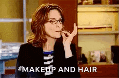 a woman wearing glasses is applying makeup to her lips and says `` makeup and hair '' .