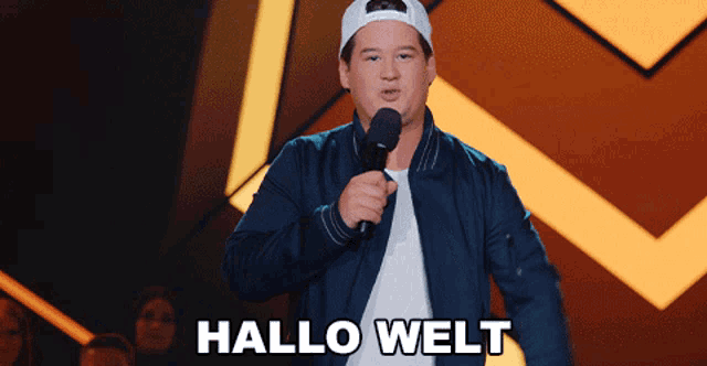 a man speaking into a microphone with the word hallo welt written below him