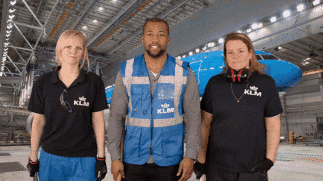 a man in a blue vest that says klm stands between two women