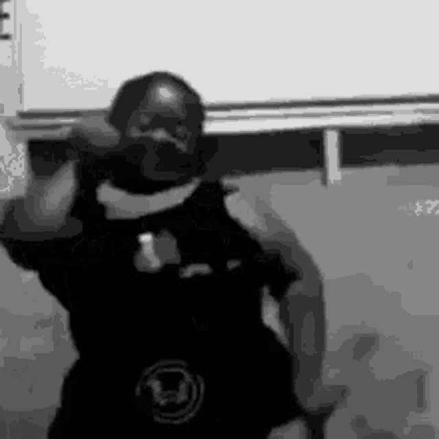 a black and white photo of a man dancing in front of a white wall .
