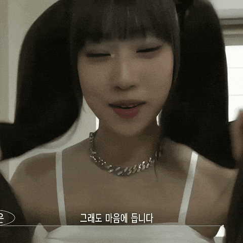a woman wearing a white tank top and a silver necklace has korean writing on her chest