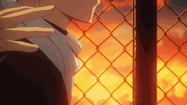 a man is standing in front of a chain link fence with a fire in the background