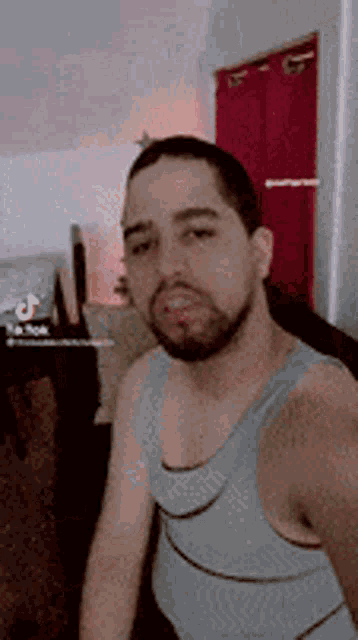 a man with a beard is wearing a tank top and taking a selfie .