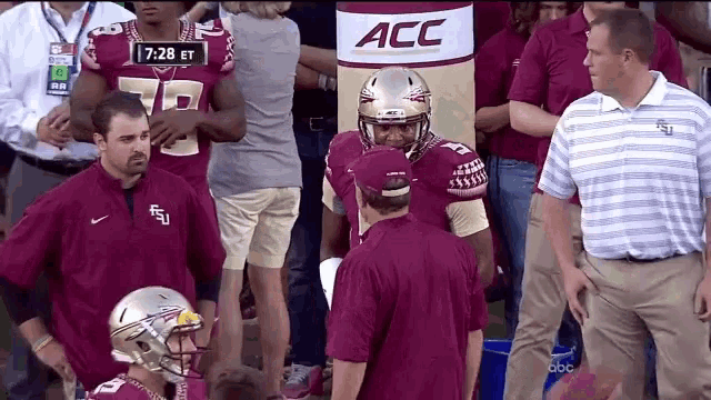 a group of football players standing in front of an acc banner
