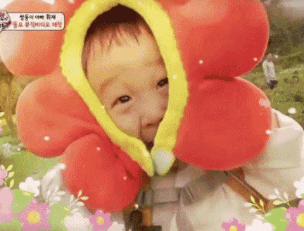 a baby wearing a flower hat is looking at the camera and smiling .