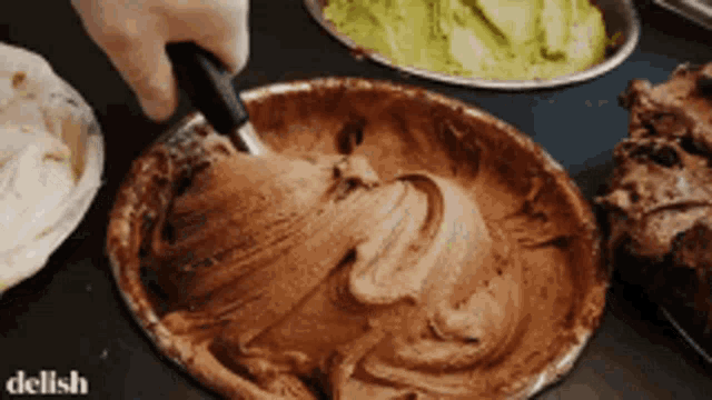 a person is stirring a bowl of chocolate ice cream with a spatula