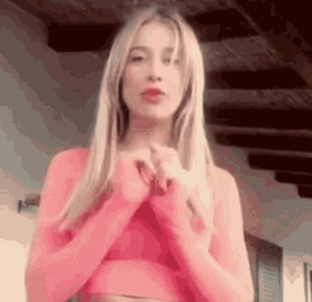 a woman in a pink crop top is standing in a room with her hands folded in front of her face .
