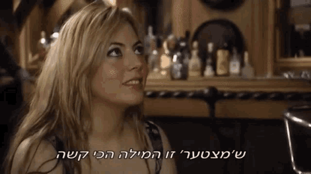 a woman is sitting at a table with bottles in the background and a caption in hebrew