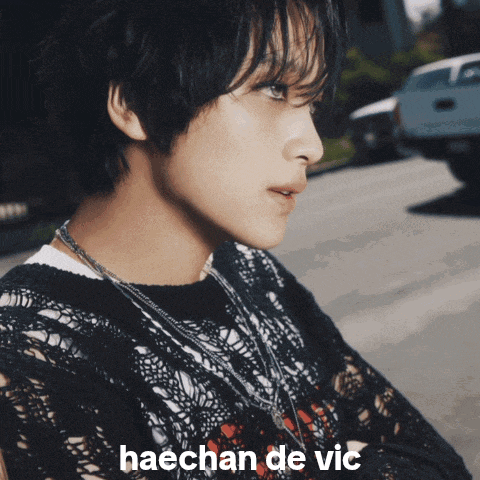 a man in a black lace shirt is standing next to a fence with the name haechan de vic written on it