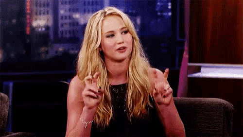 a blonde woman in a black dress is sitting on a couch and talking